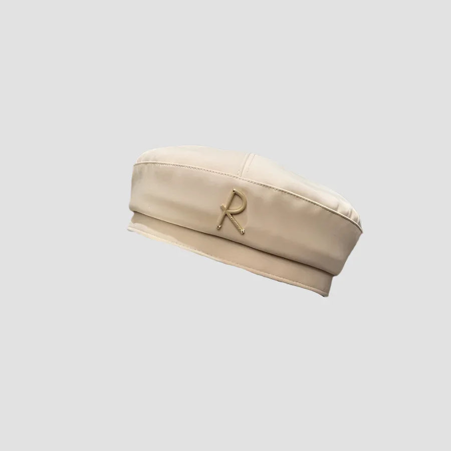 Beige beret with gold ’R’ embellishment.