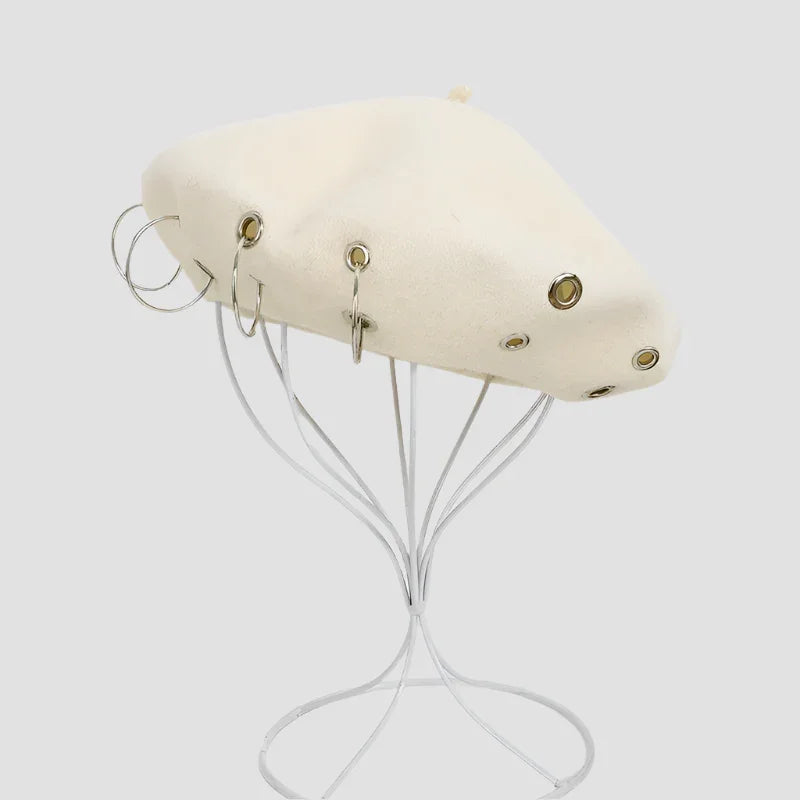 Cream-colored beret with metal grommets and hoop earrings.