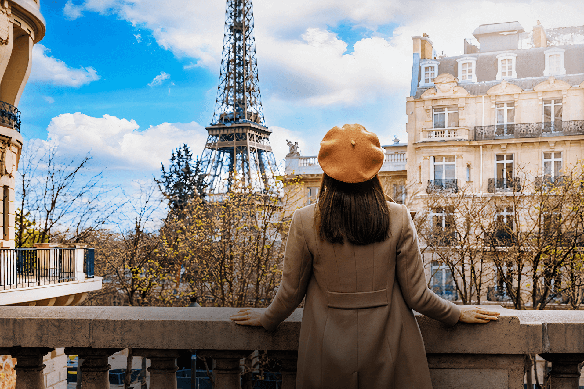 Woman wearing a brown beret looking at Eiffel Tower from a Paris balcony.