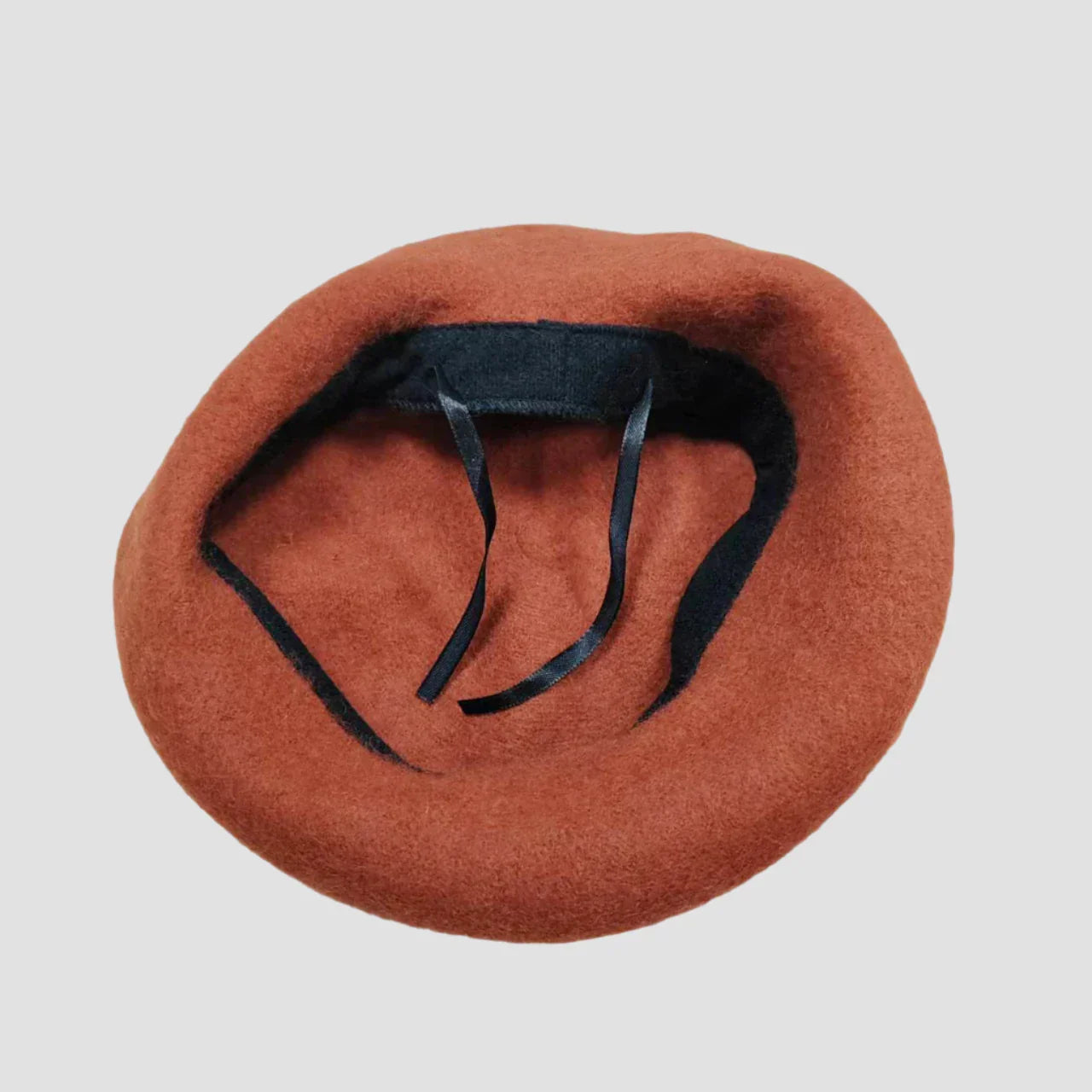 Rust-colored wool beret with black lining and ribbon ties.