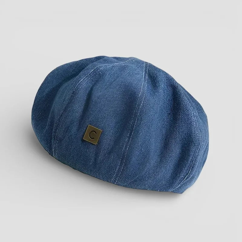 Blue denim flat cap with small square metallic logo patch