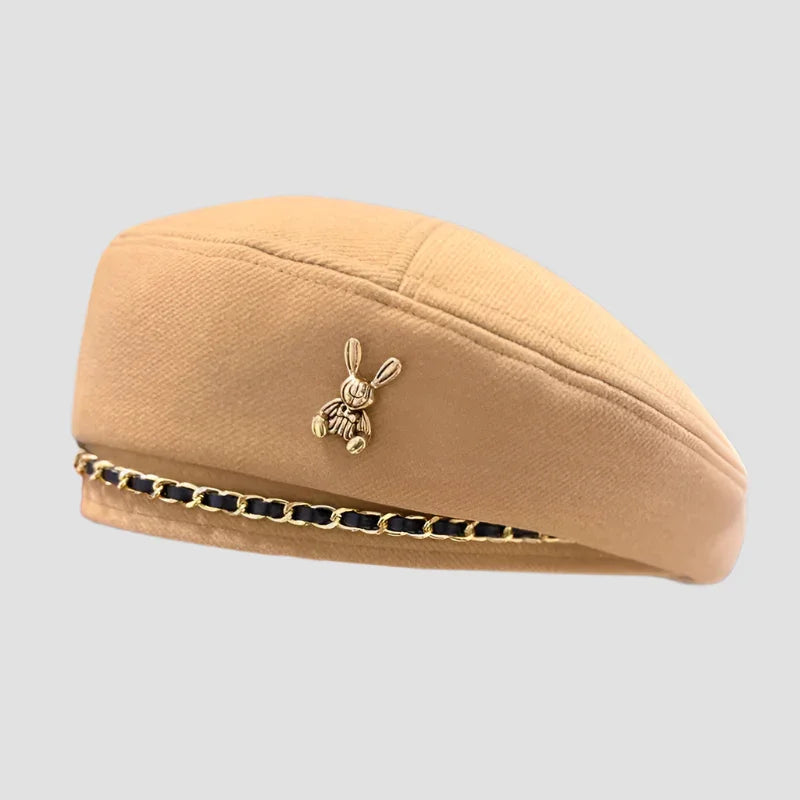 Beige beret with rabbit pin and chain detail.