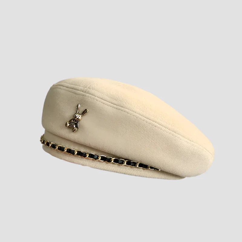Cream-colored beret with rabbit pin and chain detail.