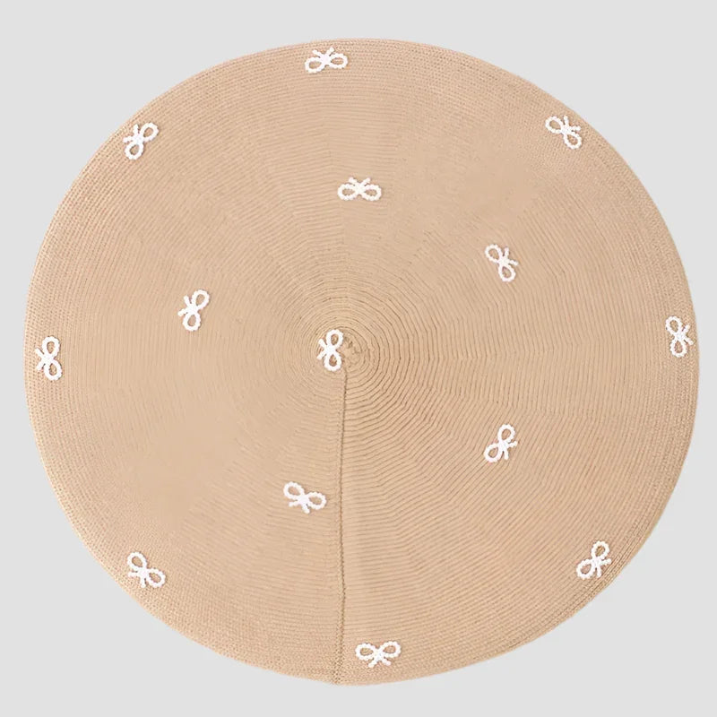 Round, tan rug with white bow accents.