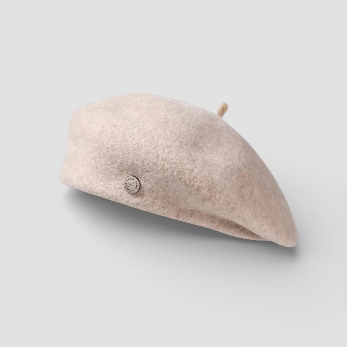 Soft blush felted wool beret with metallic emblem and textured surface