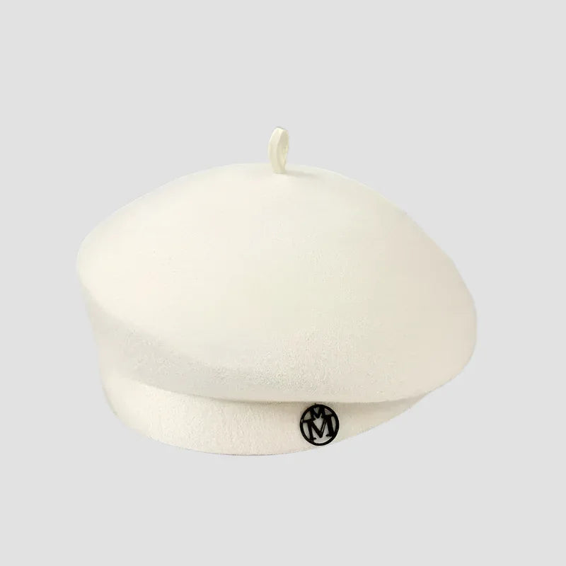 Cream-colored beret with a small loop on top and a circular emblem.