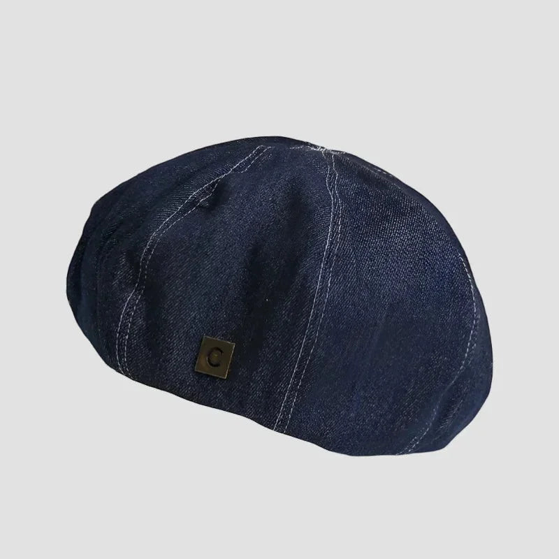 Navy blue denim beret with white stitching and metal logo patch
