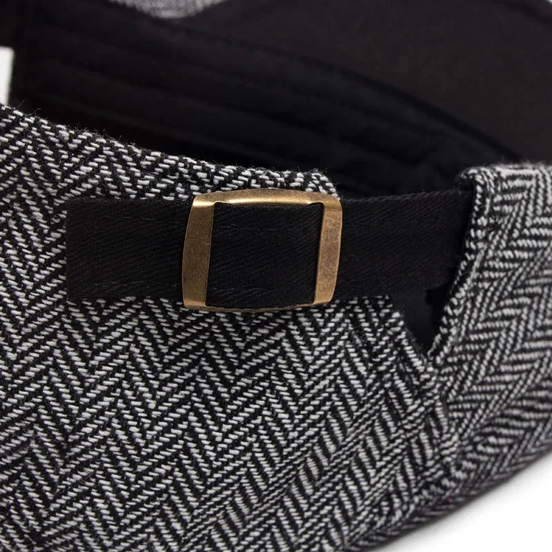 Herringbone newsboy cap with adjustable strap.
